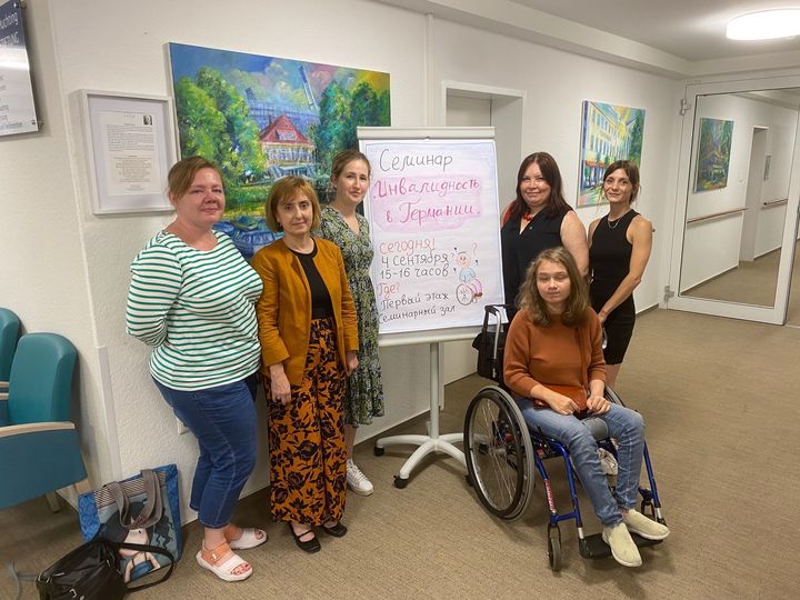 Anna Müllervom Gesundheitspunkt Huchting hat ein tolles Werbeplakat selbst gemalt.  Davor stehen auf diesem Foto eine Familie aus dem Übergangswohnheim Tegeler Plate und unsere Beraterinnen Elena Petri-Siagas und Yulia Kuhn.
