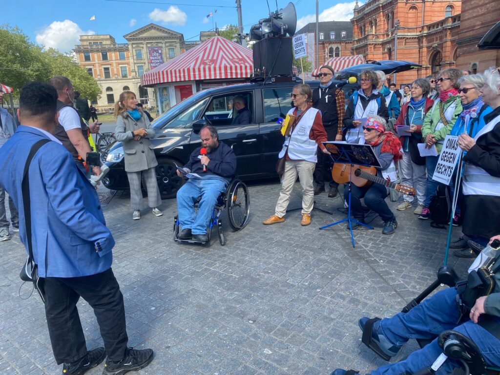 Florian Grams eröffnet den 33. Bremer Protesttag vor dem Bremer Hauptbahnhof. Er ist umringt von den Demonstrant:innen und den "Omas gegen Rechts", die zum Auftakt kämpferische Lieder gegen rechtsradikale Tendenzen gesungen haben.