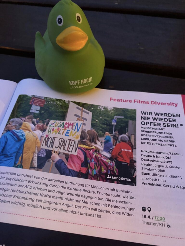 Die grüne Kautschukente der LAGS sitzt stolz und fröhlich auf der Seite des Filmfest-Programmheftes mit einem Bild und Text zum LAGS-Wettbewerbsbeitrag "Wir wollen nie wieder Opfer sein", ein Film der Compagnons mit Jürgen Köster und Liz Dinh.